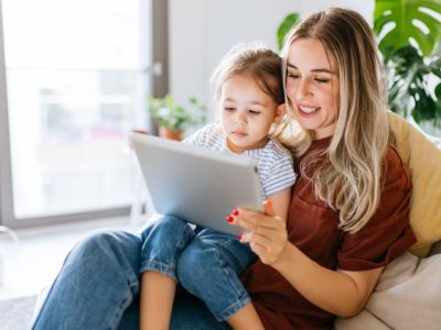 A young girl sits on her mum’s lap, watching  screens together can help with iPad tantrums