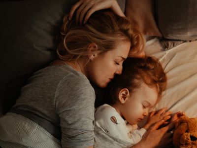 A mum and daughter cuddling in bed; positive parenting can help kids overcome sleep problems.