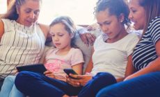 family sitting together on couch, two children are looking at devices