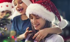Two smiling girls in Santa hats decorate a Christmas tree