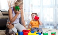 mother playing pretend telephone with little boy using building blocks