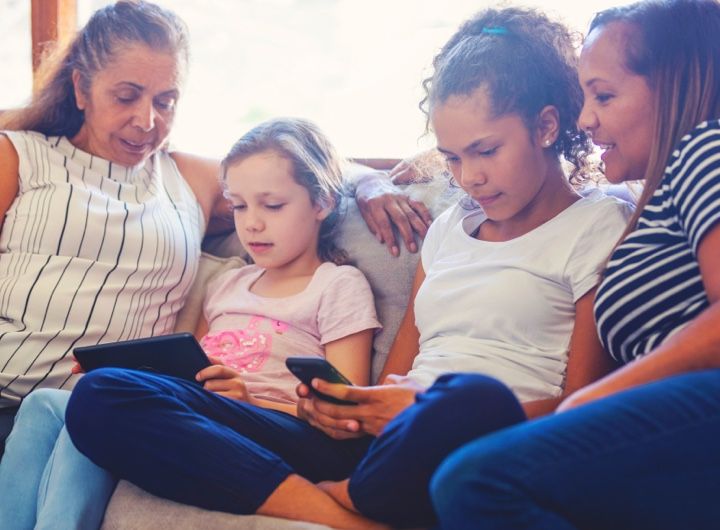 family sitting together on couch, two children are looking at devices